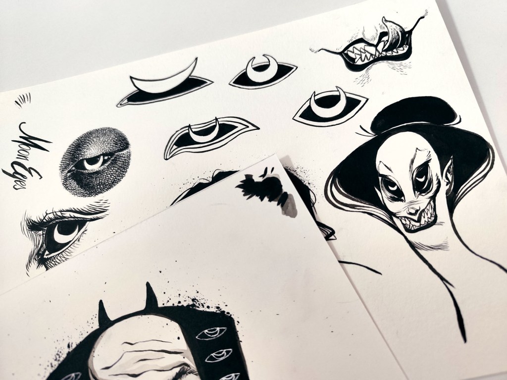 Photo of hand-drawn black-and-white ink line art sheets titled “Moon Eyes”, featuring stylized eyes with crescent moons, a sharp-toothed mouth, and a sinister long-haired creature portrait with splattered ink.