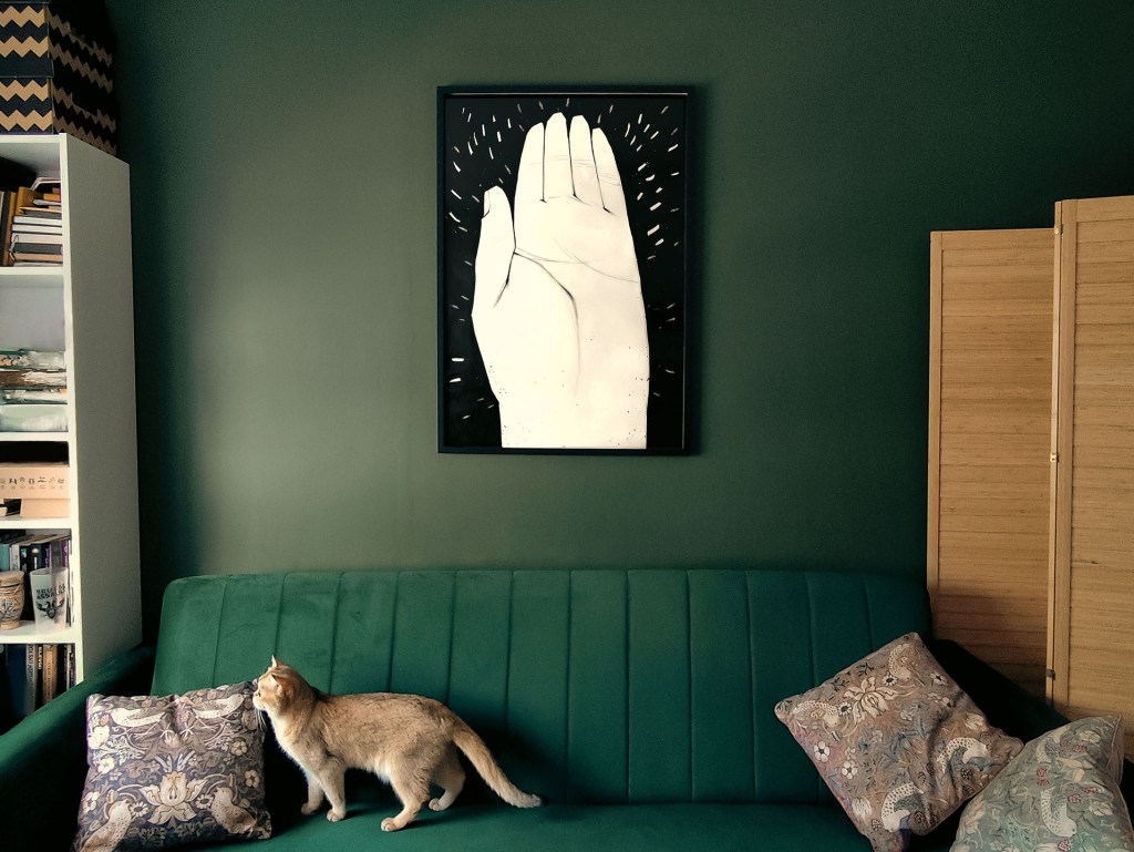 Framed Hand of Ba illustration hanging above a green sofa in a dark green room.
